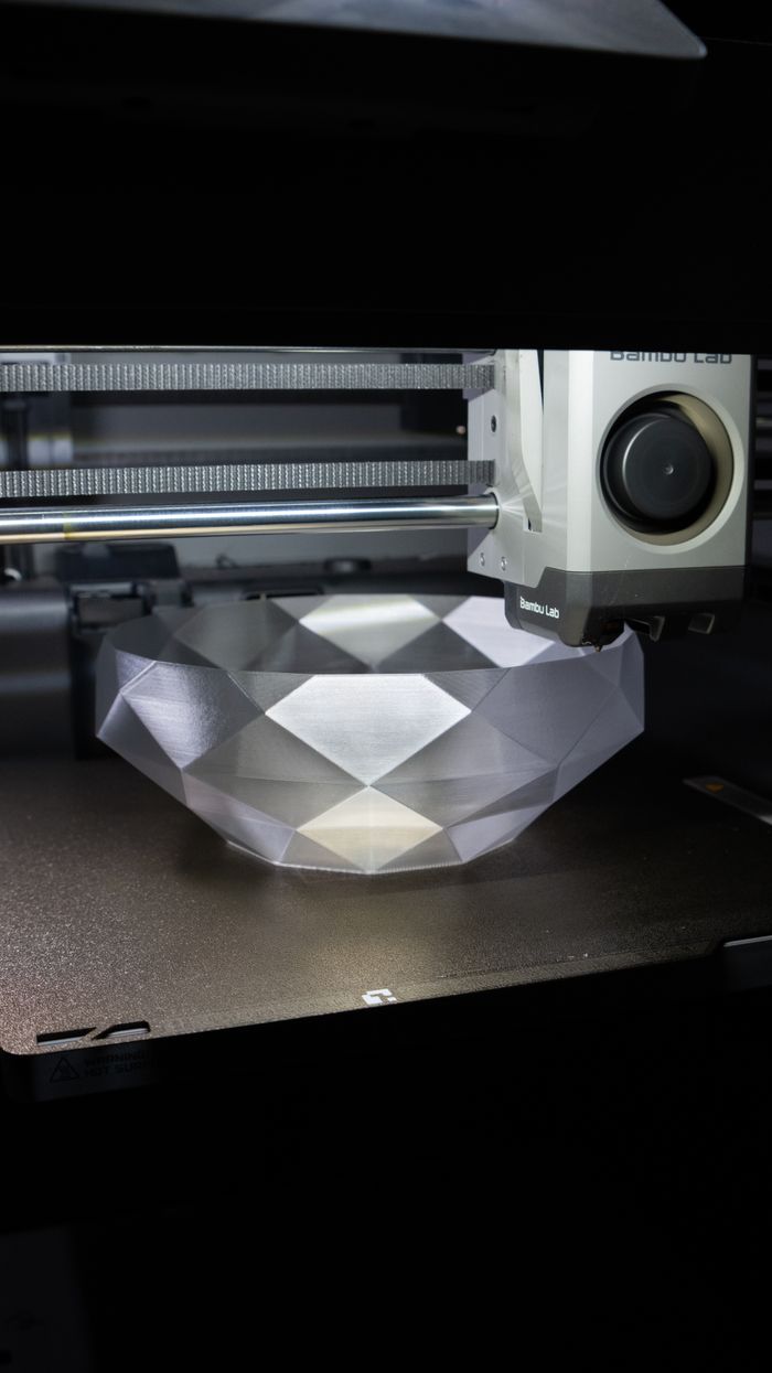 about-img A 3D printer creating a geometric crystal-like bowl in a modern setup.